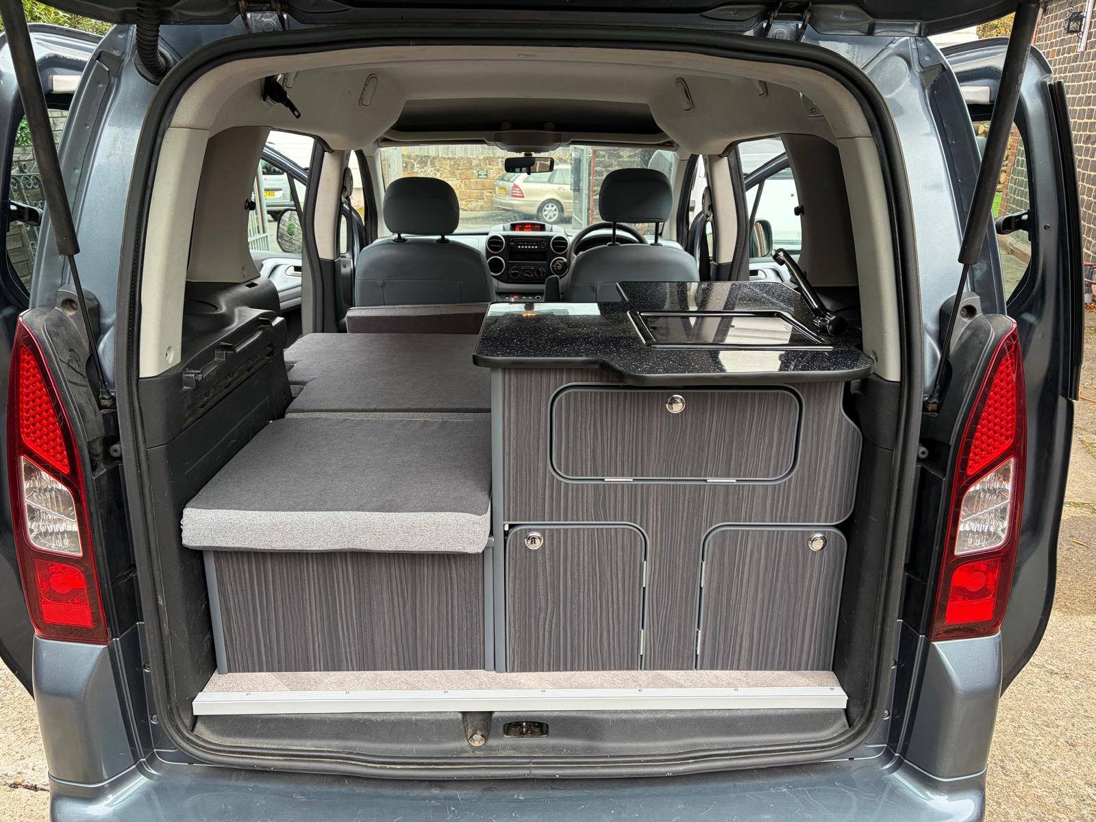 A mattress platform and a wood-effect kitchen cabinet in the boot of a van.
