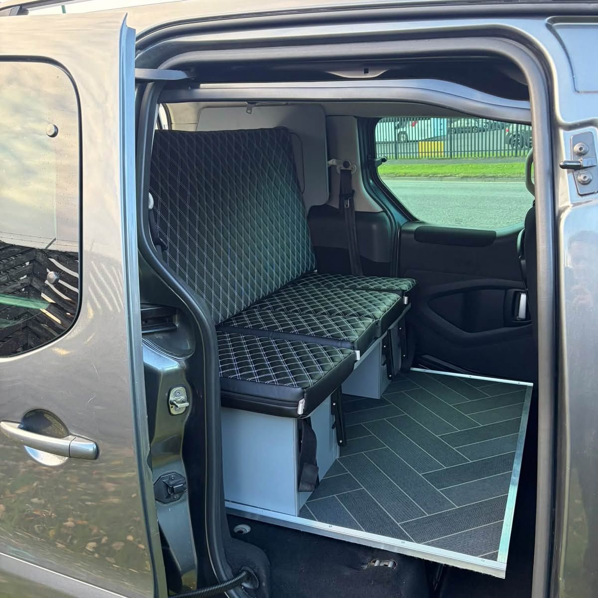 Side door open on a quilted bench seat with storage underneath and a panelled floor.